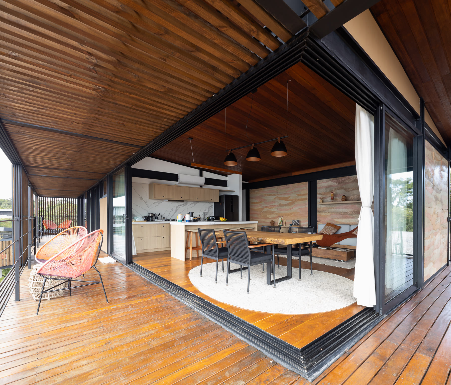 A esquina de vidro da sala aberta por inteiro, com o piso seguindo para o deck