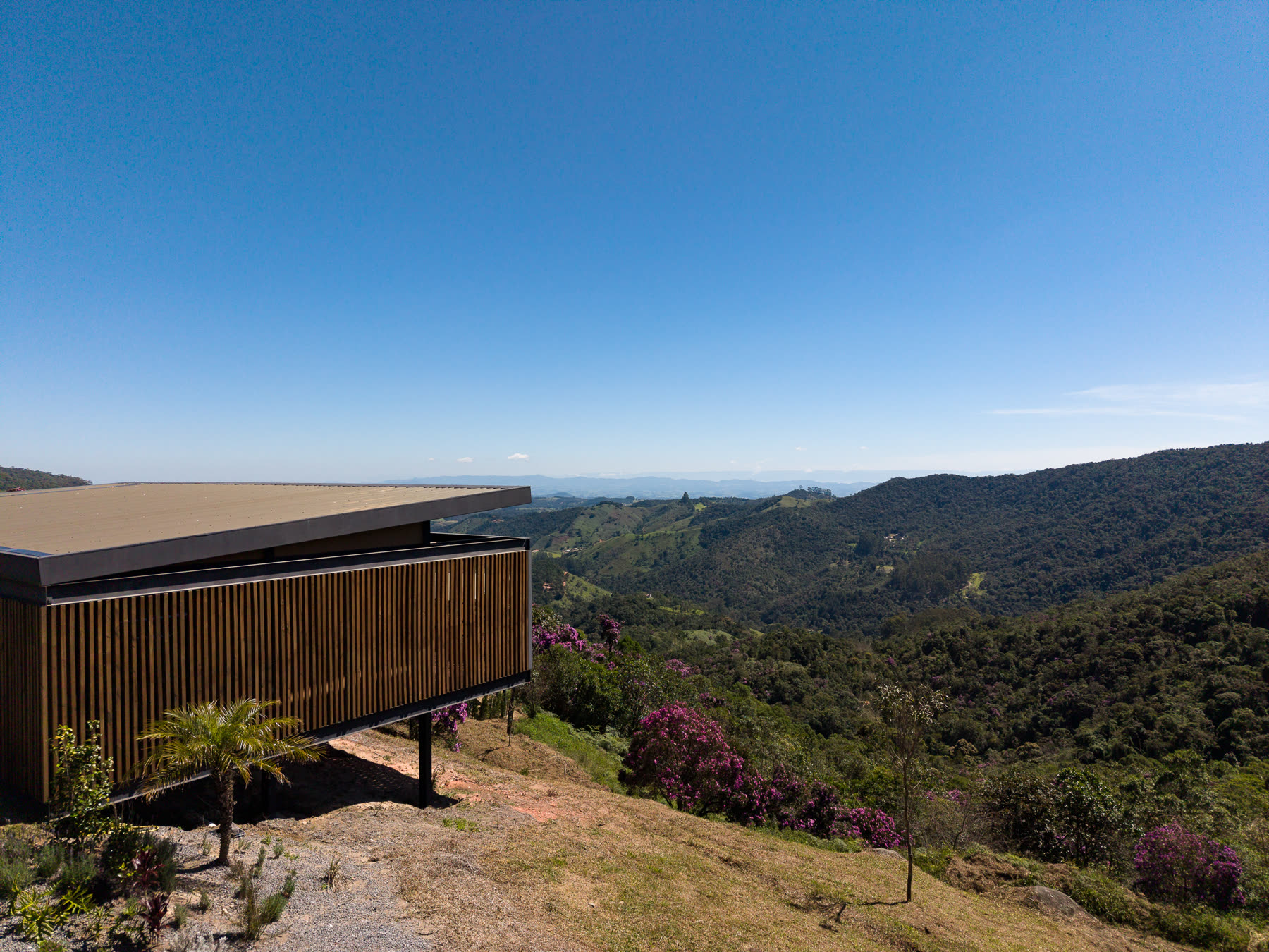 Vista aérea da casa na crista do morro, com o vale de Mata Atlântica ao fundo