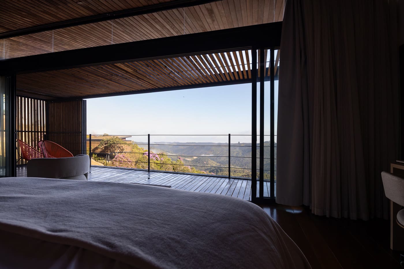 A cama de frente para a esquina de vidro aberta, com o mar de morros ao fundo