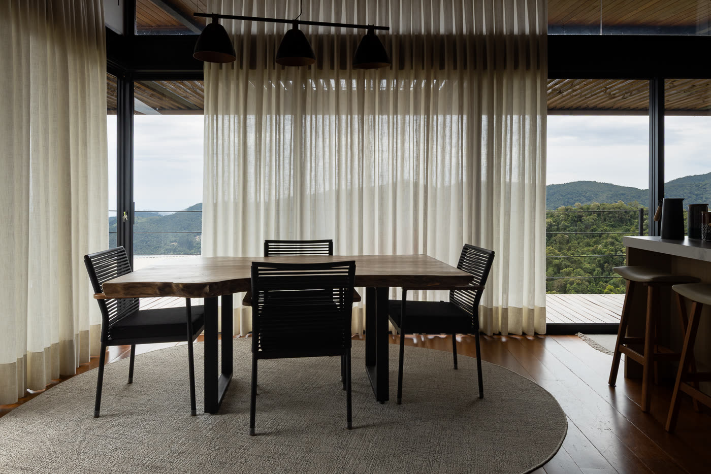 A mesa de jantar com as cortinas de voil e a serra atrás