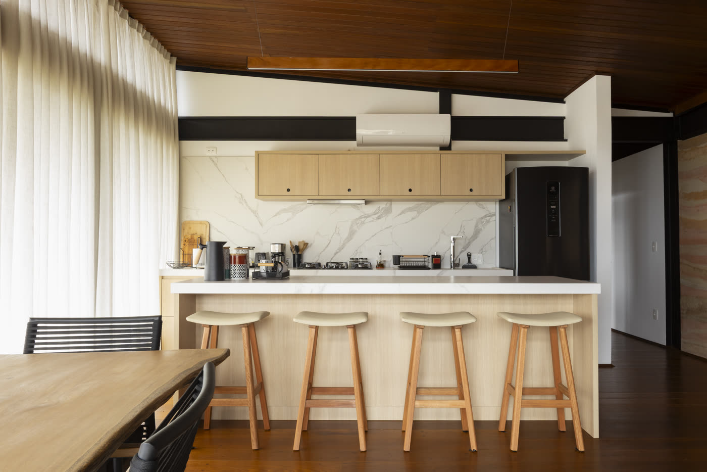 A cozinha com ilha de pedra clara e banquetas de madeira