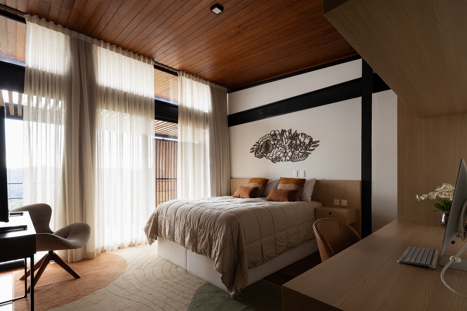 Suíte com cama queen, painel floral vazado na parede e escrivaninha