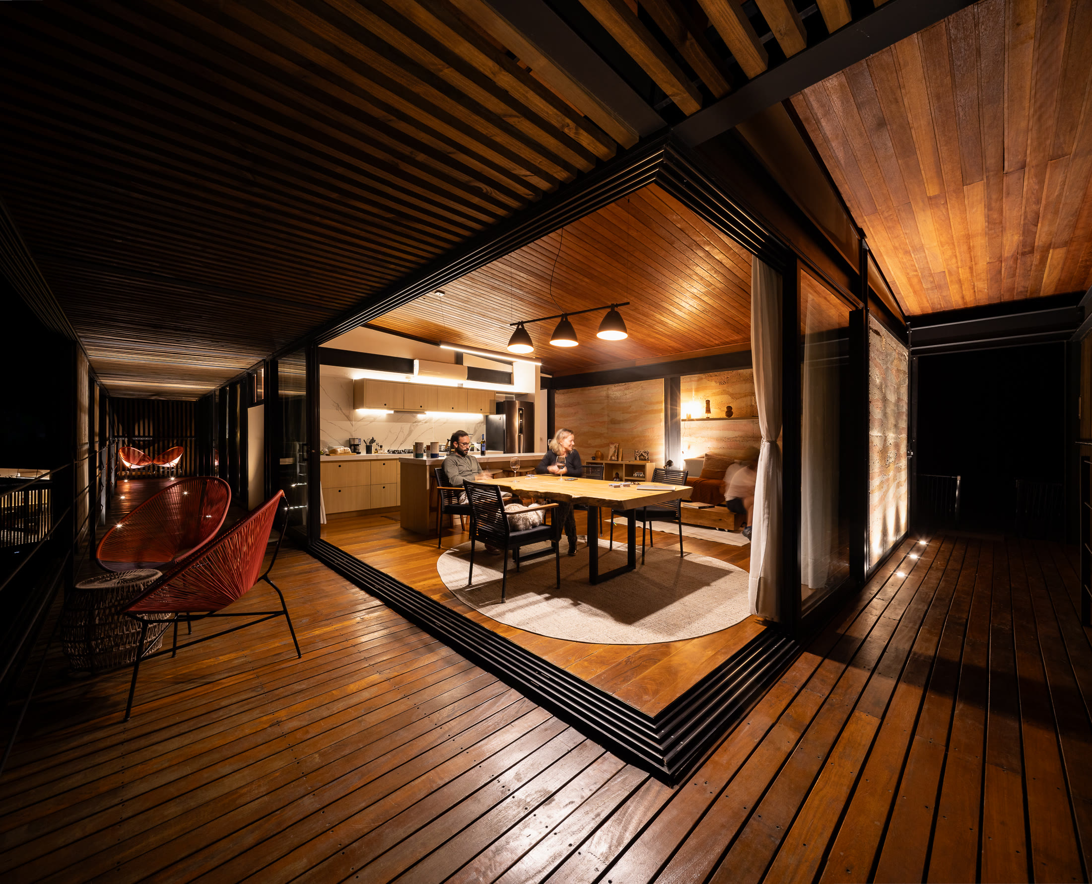 O deck ao anoitecer, com o interior da casa aceso atrás do vidro